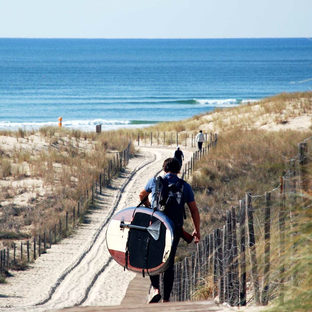 Surfer marchant vers l'océan avec sa planche sous le bras.